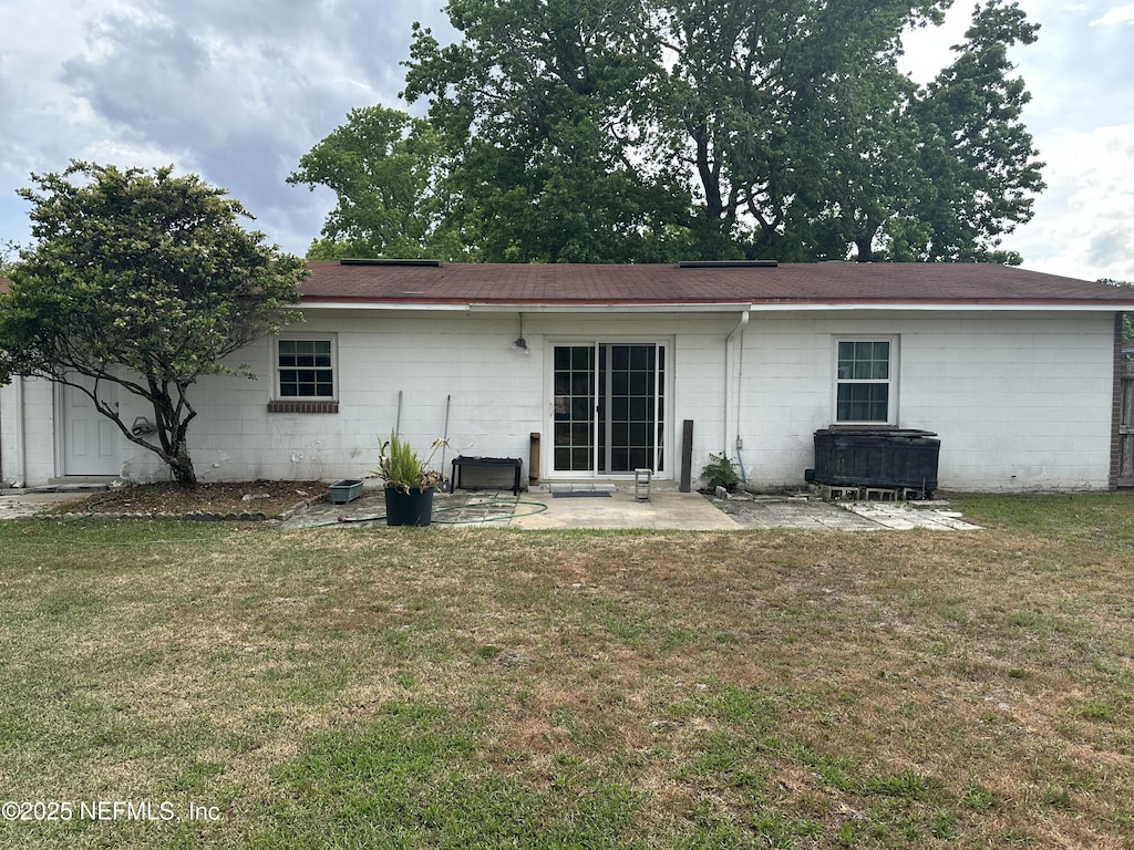 rear view of property with a yard, concrete block siding, and a patio area