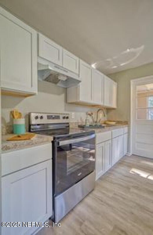 9717 Carbondale Dr W, Jacksonville, FL 32208 - kitchen with electric stove, under cabinet range hood, light wood-style flooring, light countertops, and white cabinets