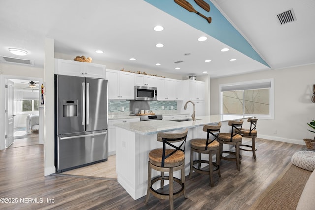 kitchen with white cabinets, a sink, a breakfast bar, stainless steel appliances, and a center island with sink