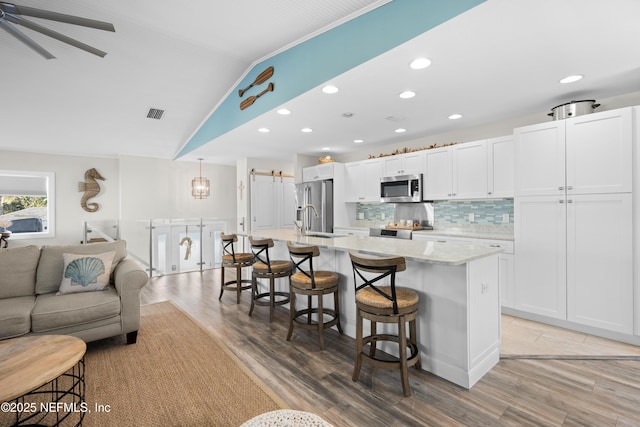 kitchen featuring a kitchen breakfast bar, white cabinets, appliances with stainless steel finishes, open floor plan, and backsplash