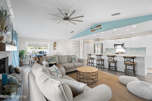 living room with light wood-style flooring, visible vents, ceiling fan, vaulted ceiling, and a brick fireplace