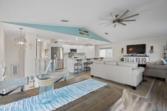 living area with visible vents, light wood-type flooring, ceiling fan with notable chandelier, and lofted ceiling