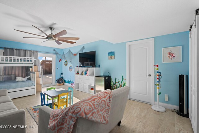 living area featuring a barn door, a ceiling fan, and baseboards