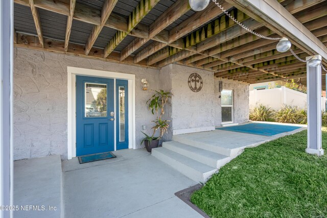 property entrance featuring a lawn, stucco siding, and fence