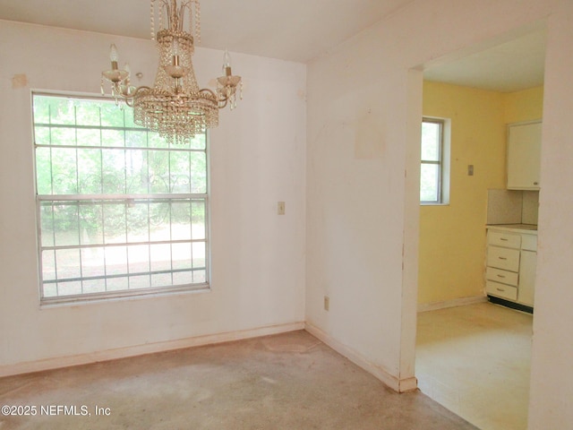 unfurnished dining area featuring light colored carpet, baseboards, and an inviting chandelier