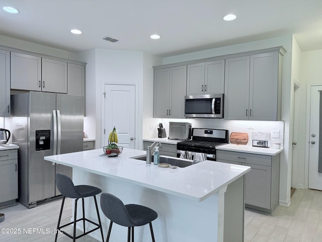 kitchen with decorative backsplash, a kitchen bar, gray cabinetry, a sink, and stainless steel appliances