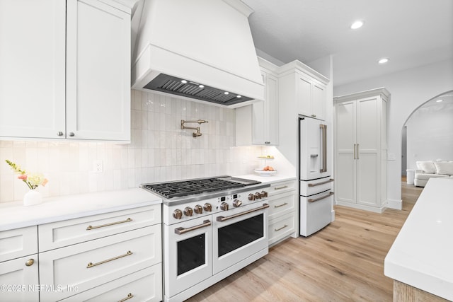 kitchen with high quality appliances, light countertops, light wood-style flooring, white cabinetry, and custom range hood