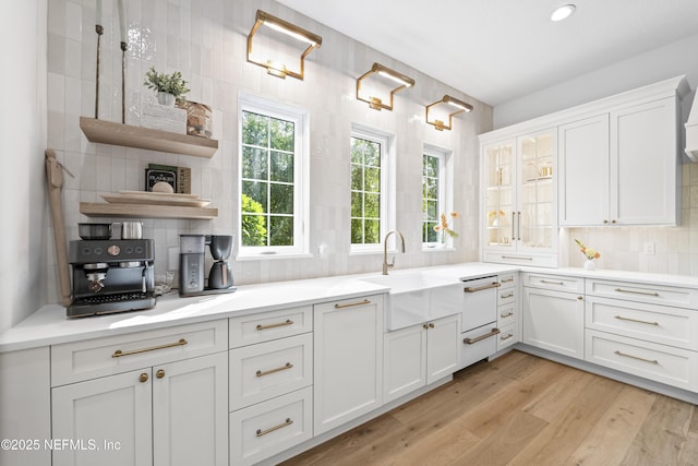 kitchen featuring decorative backsplash, light wood-type flooring, light countertops, white cabinetry, and a sink