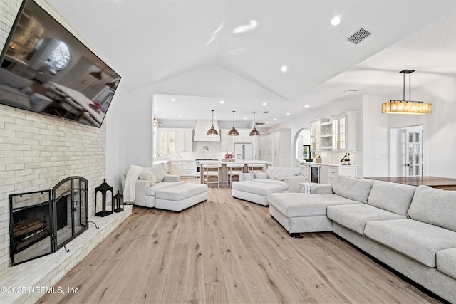 living room with a fireplace, light wood-style floors, recessed lighting, lofted ceiling, and visible vents