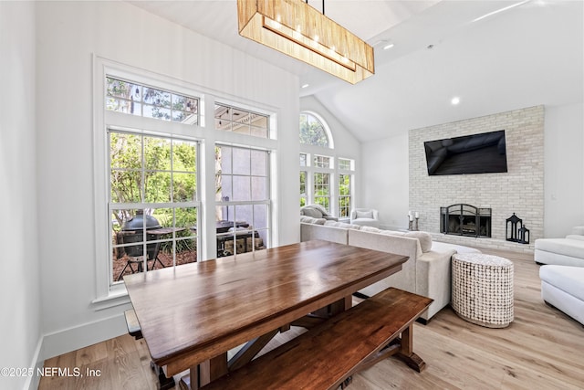 dining space featuring recessed lighting, light wood-style flooring, a brick fireplace, and high vaulted ceiling