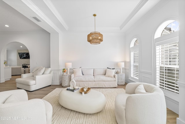 living room featuring crown molding, arched walkways, visible vents, and wood finished floors
