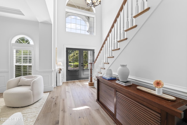 foyer featuring an inviting chandelier, stairs, wainscoting, a high ceiling, and light wood-style flooring