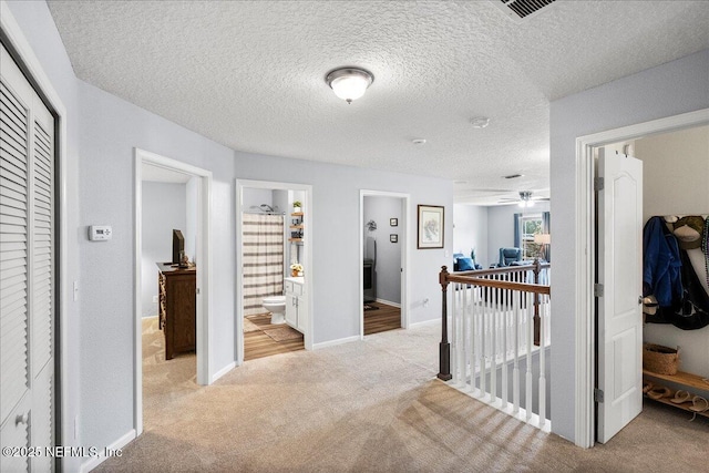 corridor featuring carpet flooring, an upstairs landing, a textured ceiling, visible vents, and baseboards