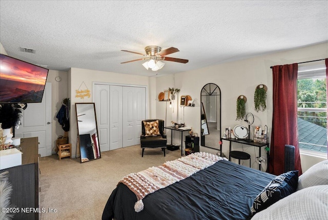 carpeted bedroom with a textured ceiling, a closet, a ceiling fan, and visible vents
