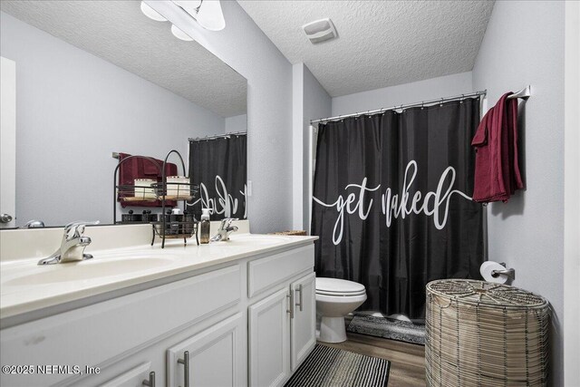 full bath featuring a textured ceiling, double vanity, a sink, and wood finished floors