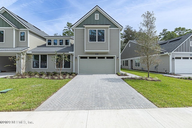 view of front of house with a shingled roof, a garage, board and batten siding, a front yard, and decorative driveway