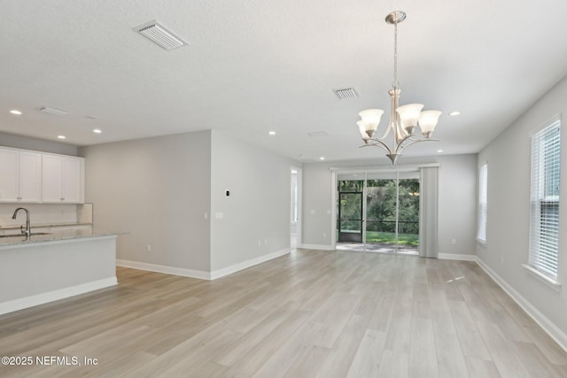 unfurnished living room with visible vents, a sink, light wood-style flooring, and an inviting chandelier