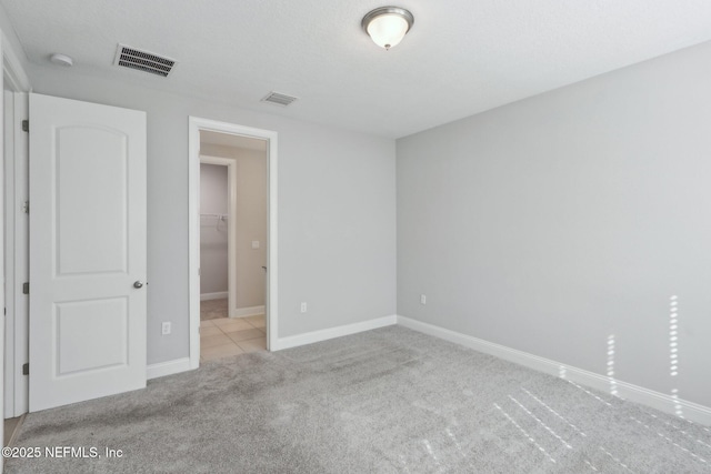 unfurnished bedroom with a spacious closet, baseboards, carpet flooring, and visible vents