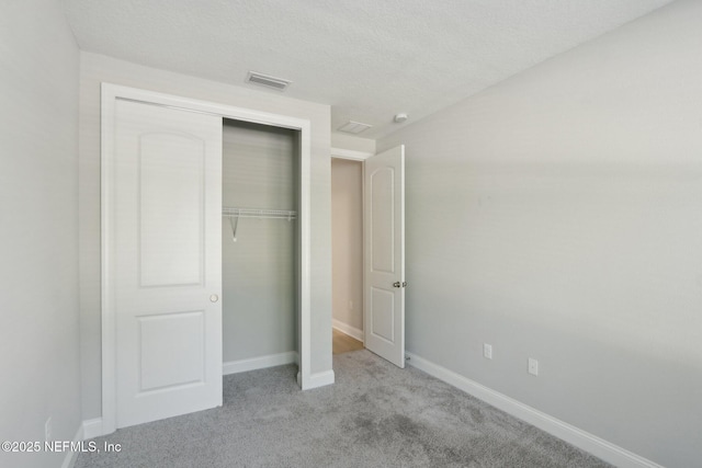 unfurnished bedroom featuring a textured ceiling, carpet, baseboards, visible vents, and a closet