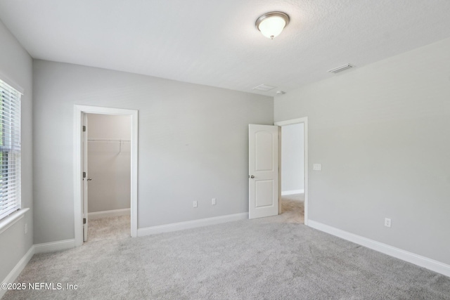 unfurnished bedroom with a spacious closet, baseboards, carpet flooring, and visible vents
