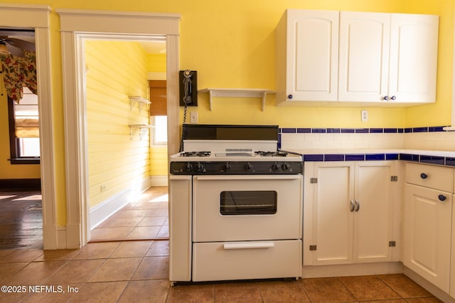 703 Emmett St, Palatka, FL 32177 - kitchen featuring white gas range oven, baseboards, white cabinets, and tile countertops