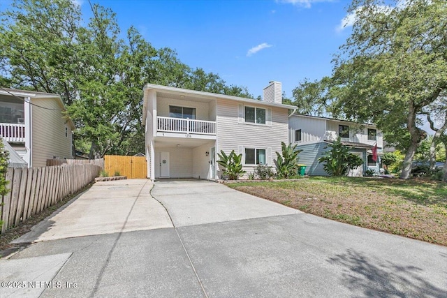 view of front of property with a chimney, a carport, fence, a balcony, and concrete driveway