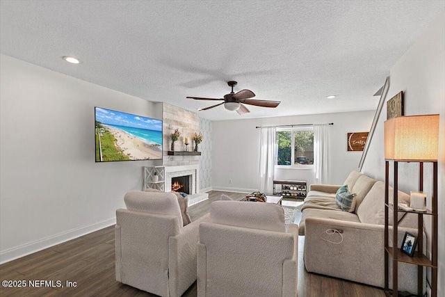 living area featuring baseboards, a ceiling fan, a stone fireplace, and dark wood-type flooring