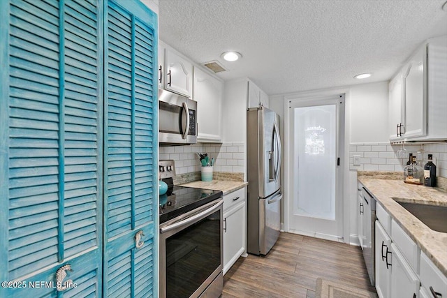 kitchen featuring visible vents, wood finished floors, a textured ceiling, white cabinetry, and stainless steel appliances