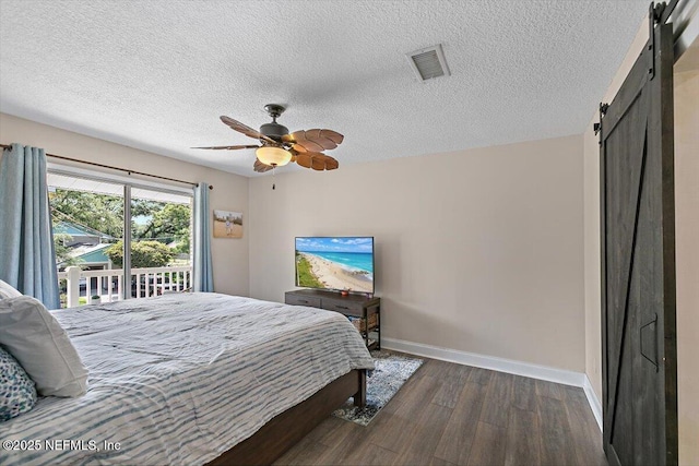 bedroom featuring visible vents, dark wood-style flooring, baseboards, a barn door, and a textured ceiling