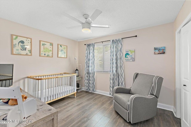 bedroom with baseboards, a textured ceiling, wood finished floors, and a nursery area