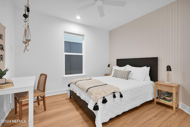 bedroom with an accent wall, wallpapered walls, light wood-style flooring, and baseboards