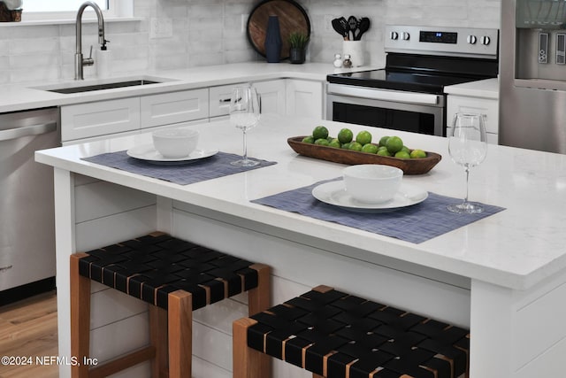 kitchen with white cabinetry, stainless steel appliances, light stone counters, and a sink