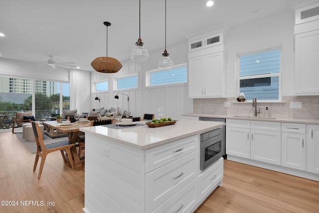kitchen with stainless steel microwave, decorative backsplash, a sink, light wood-style floors, and a center island