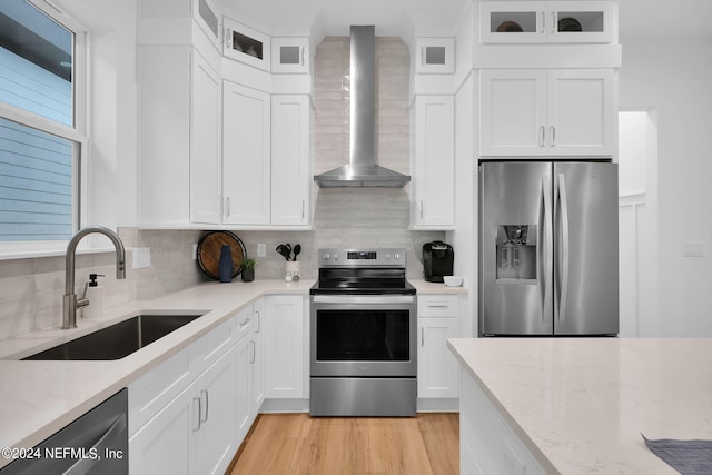 kitchen featuring light stone countertops, a sink, stainless steel appliances, backsplash, and wall chimney range hood