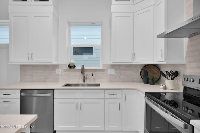 kitchen with tasteful backsplash, stainless steel appliances, wall chimney range hood, white cabinets, and a sink