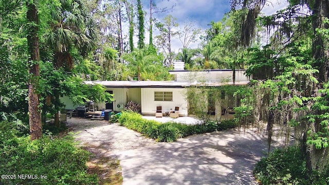 back of property featuring driveway, a chimney, and a patio area