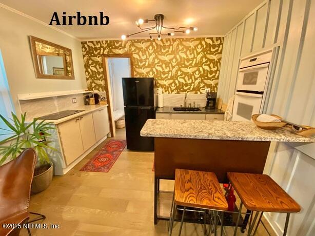 kitchen featuring white cabinets, a sink, wallpapered walls, black appliances, and a peninsula