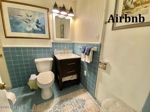 bathroom with toilet, tile patterned flooring, tile walls, and wainscoting