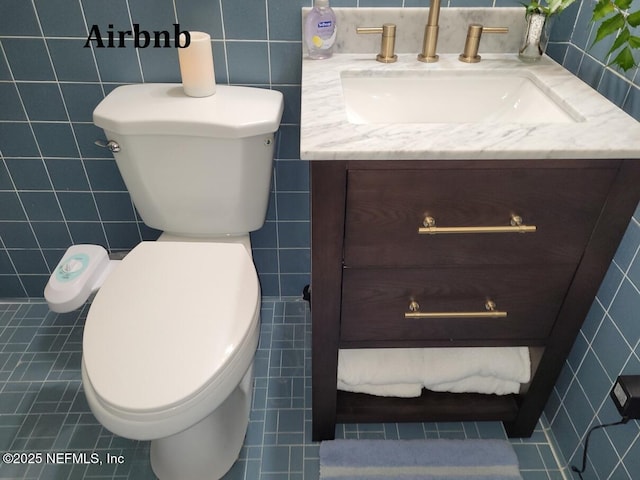 half bath with tile walls, tile patterned floors, toilet, and vanity