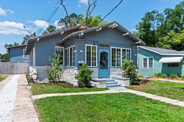 bungalow featuring fence, stucco siding, and a front lawn
