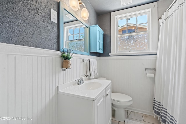 bathroom with vanity, visible vents, marble finish floor, toilet, and a wainscoted wall
