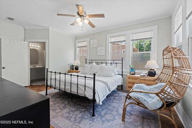 bedroom with visible vents, crown molding, dark wood-style flooring, baseboards, and connected bathroom