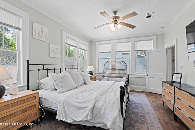 bedroom featuring ceiling fan, a textured ceiling, dark wood finished floors, visible vents, and ornamental molding