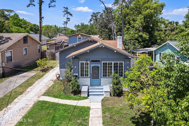 bungalow-style home with stone siding, fence, a front yard, and a chimney