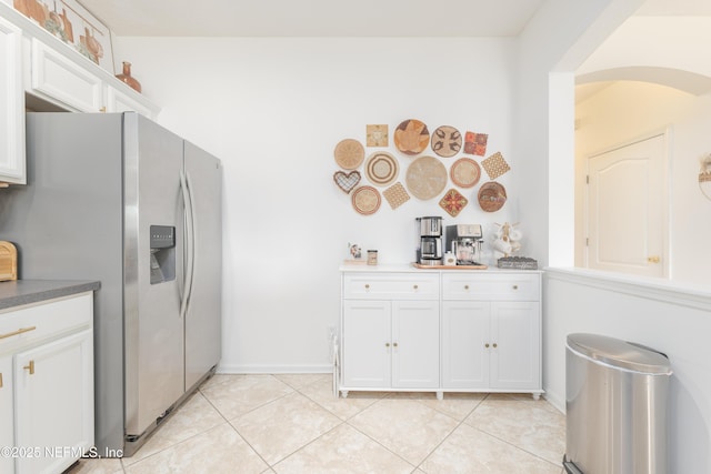 kitchen featuring arched walkways, light tile patterned floors, stainless steel fridge, white cabinets, and baseboards