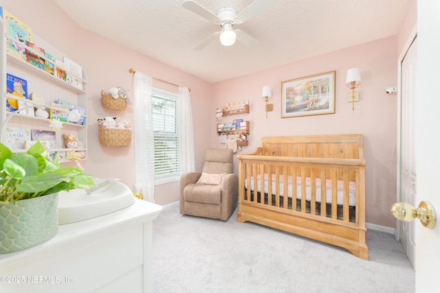 carpeted bedroom with a textured ceiling, ceiling fan, a crib, and baseboards