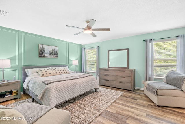 bedroom featuring a decorative wall, light wood-style floors, and ceiling fan
