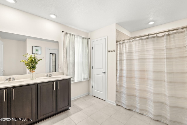 full bath featuring double vanity, baseboards, tile patterned floors, and a textured ceiling