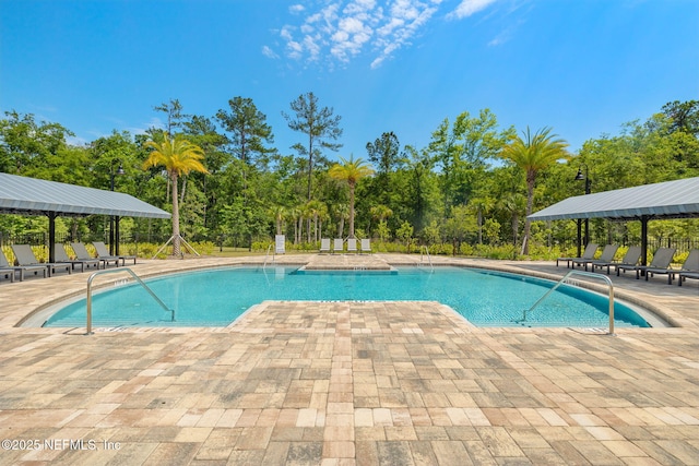 community pool featuring a patio, fence, and view of wooded area