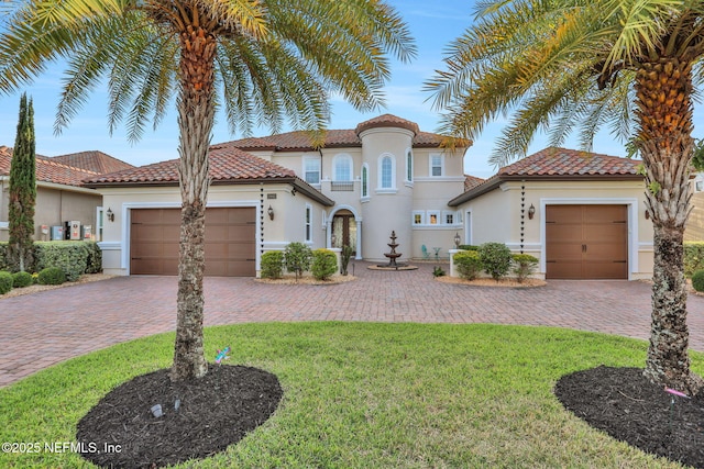 mediterranean / spanish-style house featuring stucco siding, decorative driveway, a front yard, and a garage